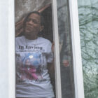 Keeshemah Johnson peers out the window of the home she once shared with her partner, Maurice Austin. Her T-shirt pays tribute to Austin.